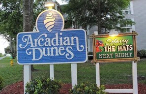 Schild für 'Acadian Dunes' mit Logo und ein weiteres Schild für 'Harry The Hats', das einen nahegelegenen Ort anzeigt.