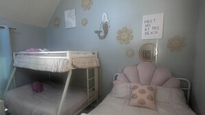 Een slaapkamer met stapelbedden, een muur versierd met bloemen en een bord waarop staat 'MEET ME AT THE BEACH'.