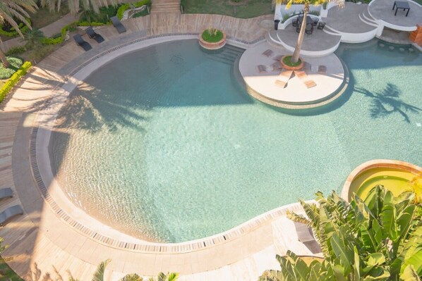 Ein runder Pool mit einer umlaufenden Sonnenterrasse, Liegestühlen und einem kleinen Gartenbereich.