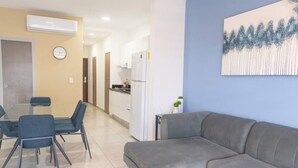 Een moderne woonkamer met een grijze bank, een eettafel met stoelen, een keuken en een klok aan de muur.