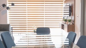 Een vergaderruimte met een glazen tafel, vier stoelen, een plafondventilator en jaloezieën.
