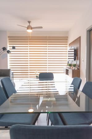 Ein Konferenzraum mit Glastisch, vier Stühlen, Deckenventilator und Jalousien.