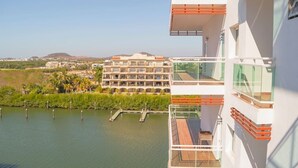 Een modern hotel met meerdere balkons met uitzicht op een waterpartij en een complex van gebouwen in de verte.