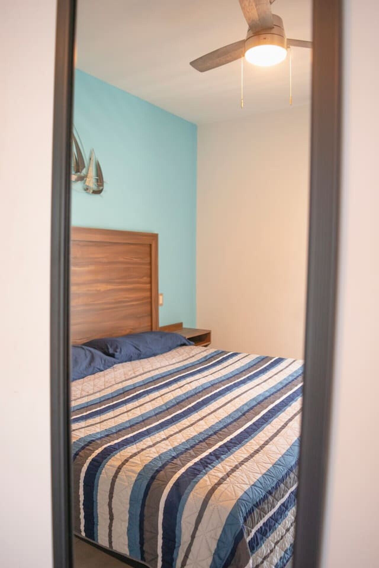 A bedroom with a bed, a wooden headboard, a ceiling fan, and a wall-mounted light fixture.