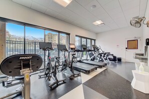 Ein Fitnessstudio mit unterschiedlichen Trainingsgeräten, großen Fenstern und Blick auf Gebäude.