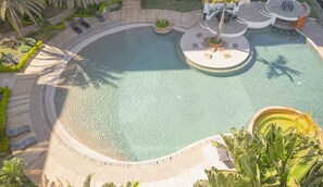 Ein kreisförmiger Pool mit einer umlaufenden Terrasse, Palmen und Sitzgelegenheiten im Freien.