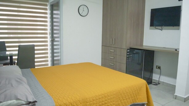 A bedroom with a bed, a desk, a television, and a clock. - Departamento Marina · Alberca · Balcón · Cerritos (Mazatlán)