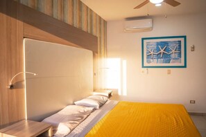 Een slaapkamer met een bed, een plafondventilator, een airconditioning en een ingelijst schilderij aan de muur.