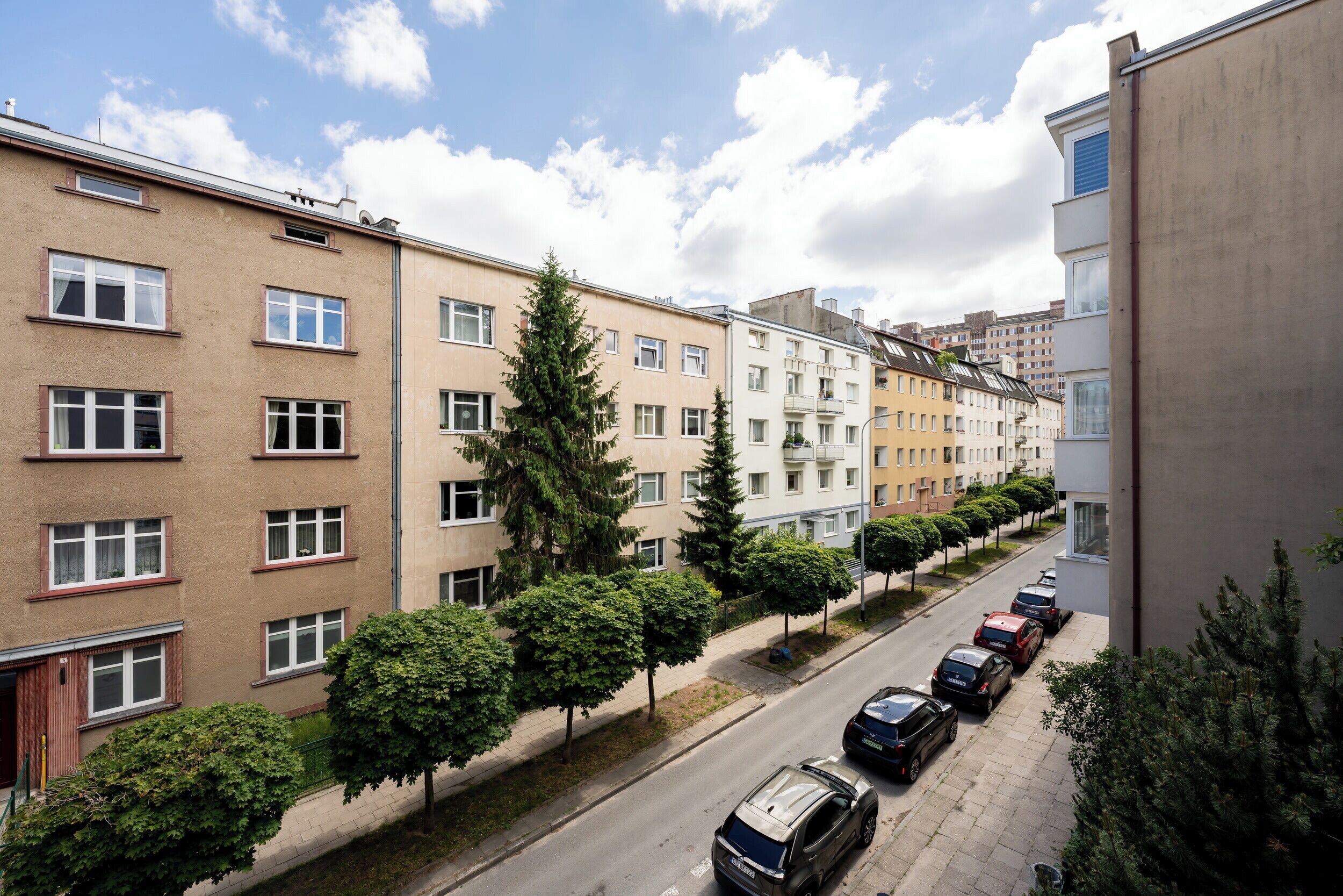 Une rangée d’immeubles résidentiels à plusieurs étages, avec des voitures garées le long de la rue.