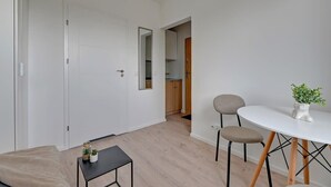 Een moderne kamer met een bank, een klein tafeltje met een plant, een ronde tafel met stoelen, en een deur die naar een keuken leidt.