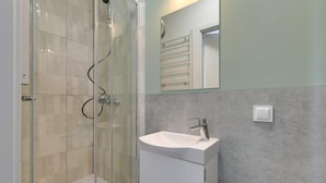 Een badkamer met een douchecabine van glas, een witte wastafel en een spiegel boven de wastafel.
