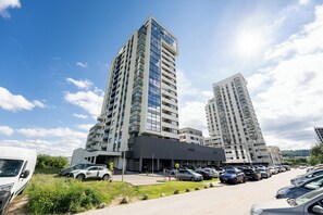 A modern building with multiple floors, a parking lot with several cars, and a clear sky.