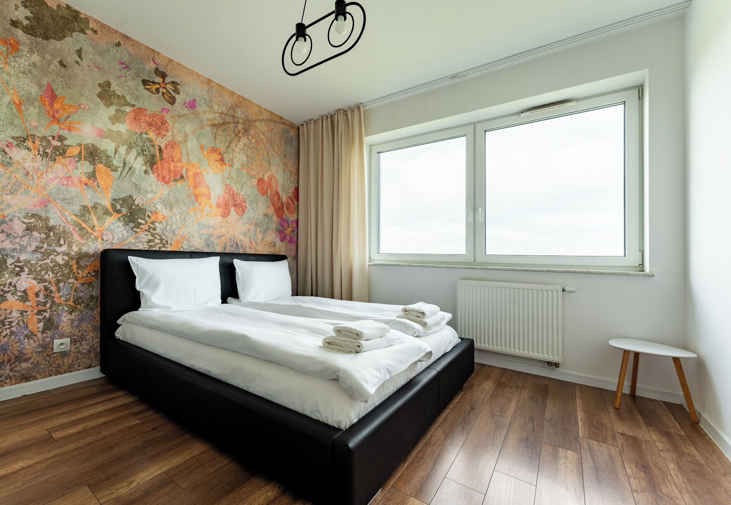 Ein modernes Schlafzimmer mit einem großen Bett, einem Heizkörper, einem Fenster und einer Wand mit einem Blumenmuster.