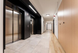A modern hallway with elevators, a tiled floor, and a wooden wall.