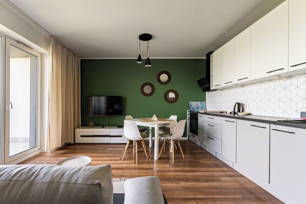 Une cuisine moderne avec des meubles blancs, un coin repas doté d’une table et de chaises blanches, et une grande fenêtre agrémentée de rideaux.