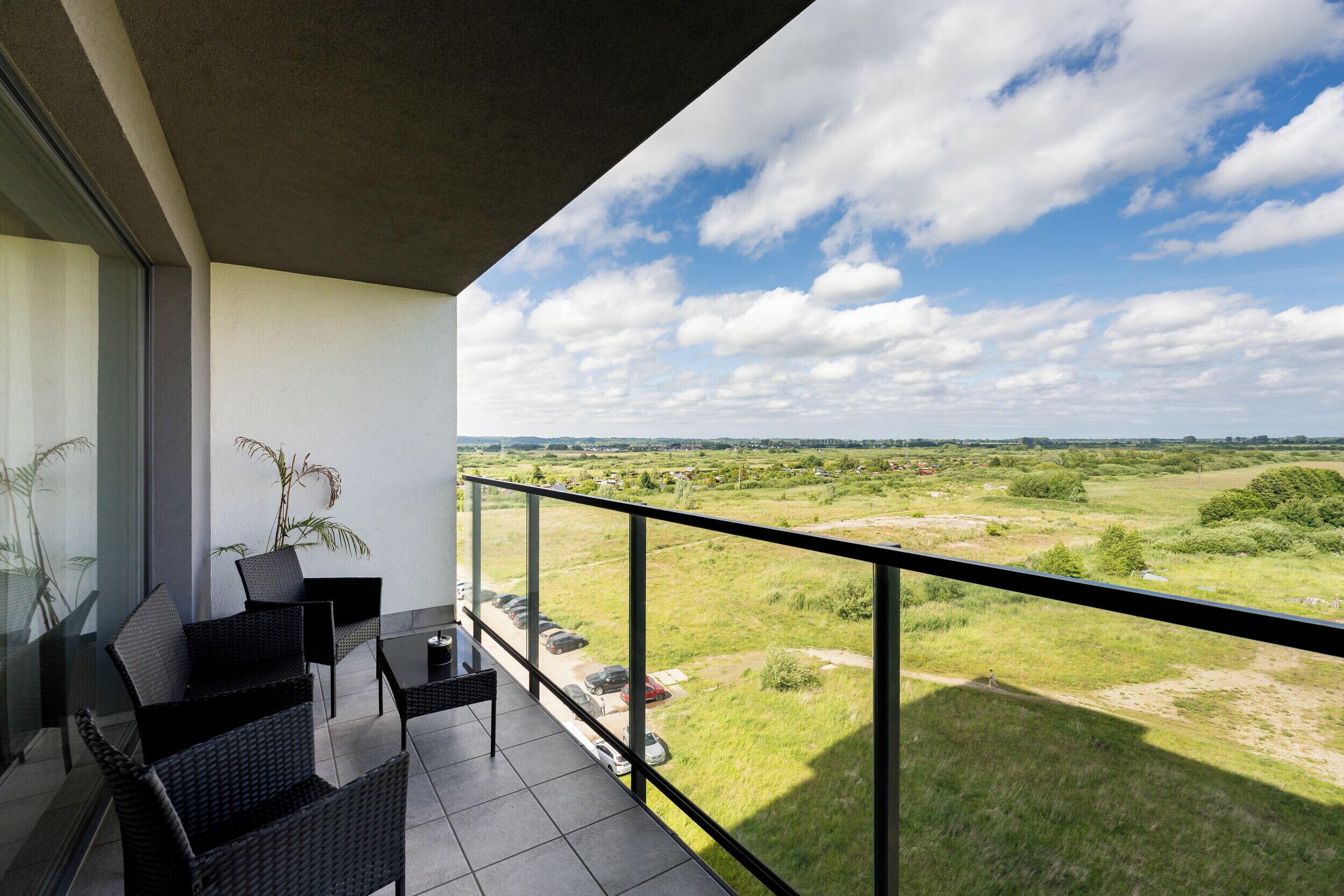 A balcony with wicker furniture, a glass door, and a view of a green landscape.