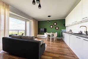 Un salon moderne avec un canapé, une table à manger et des chaises, une cuisine dotée de meubles blancs et une grande fenêtre avec des rideaux.