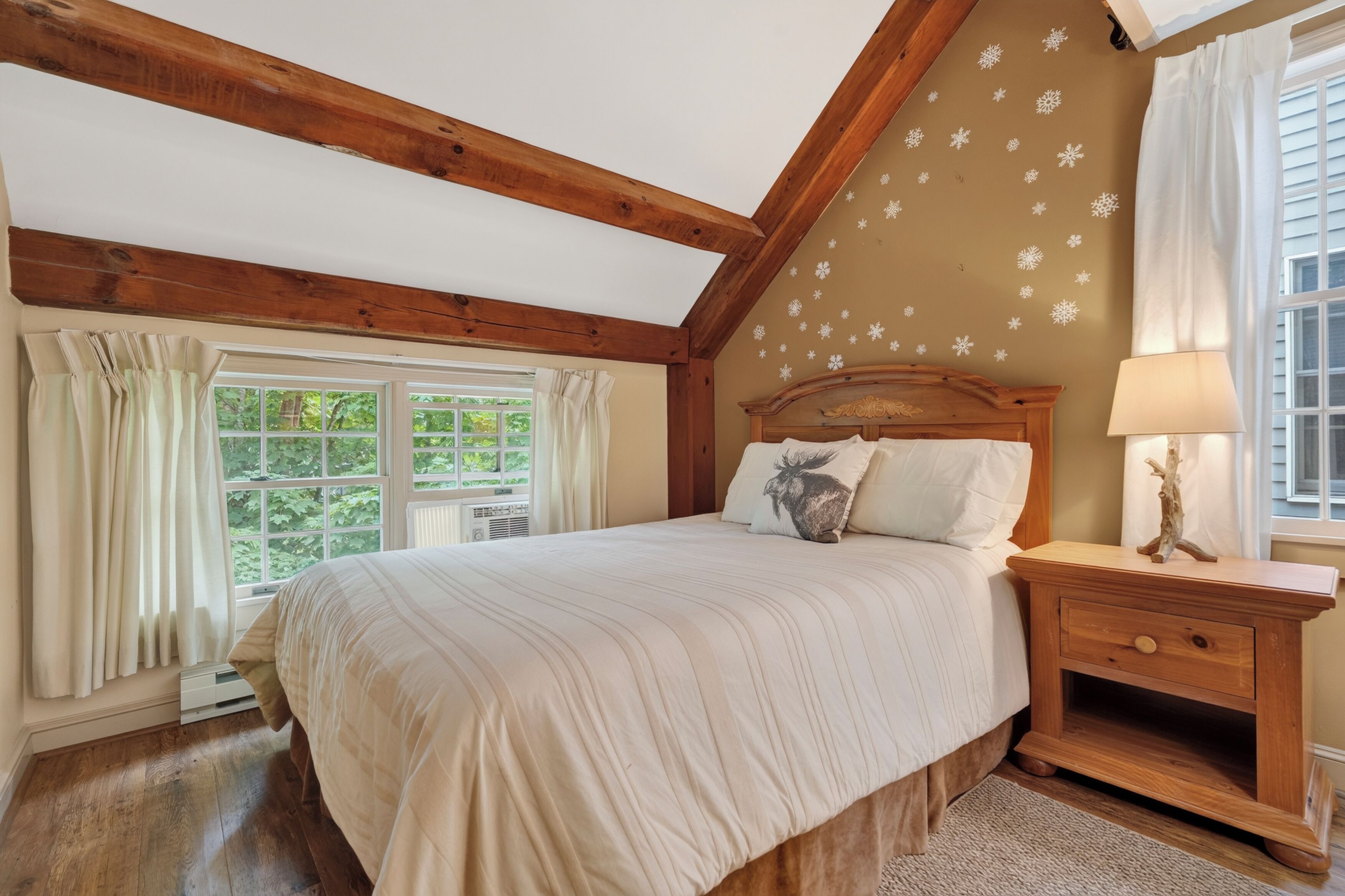 A bedroom with a wooden ceiling, a bed with a headboard, a nightstand, a window with curtains, and a wall with snowflake decals.