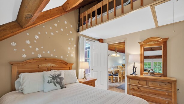Une chambre à coucher avec une tête de lit en bois, un lit recouvert d’une literie blanche, une commode, un miroir et un plafond décoré de motifs de flocons de neige.