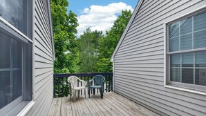Une terrasse en bois avec deux chaises, une rambarde et une vue sur les arbres.