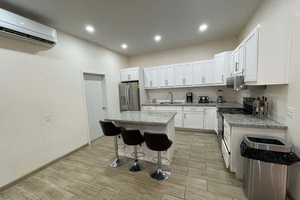 A wide-angle interior perspective capturing the kitchen from a rear viewpoint inside La Kasa #1, showcasing the full counter layout, cabinetry, and modern appliances.