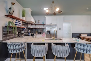A modern kitchen with a marble island, bar stools, a refrigerator, and a dining area.