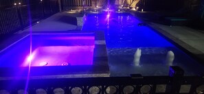 A swimming pool with a fountain feature, surrounded by a stone deck and a metal railing.