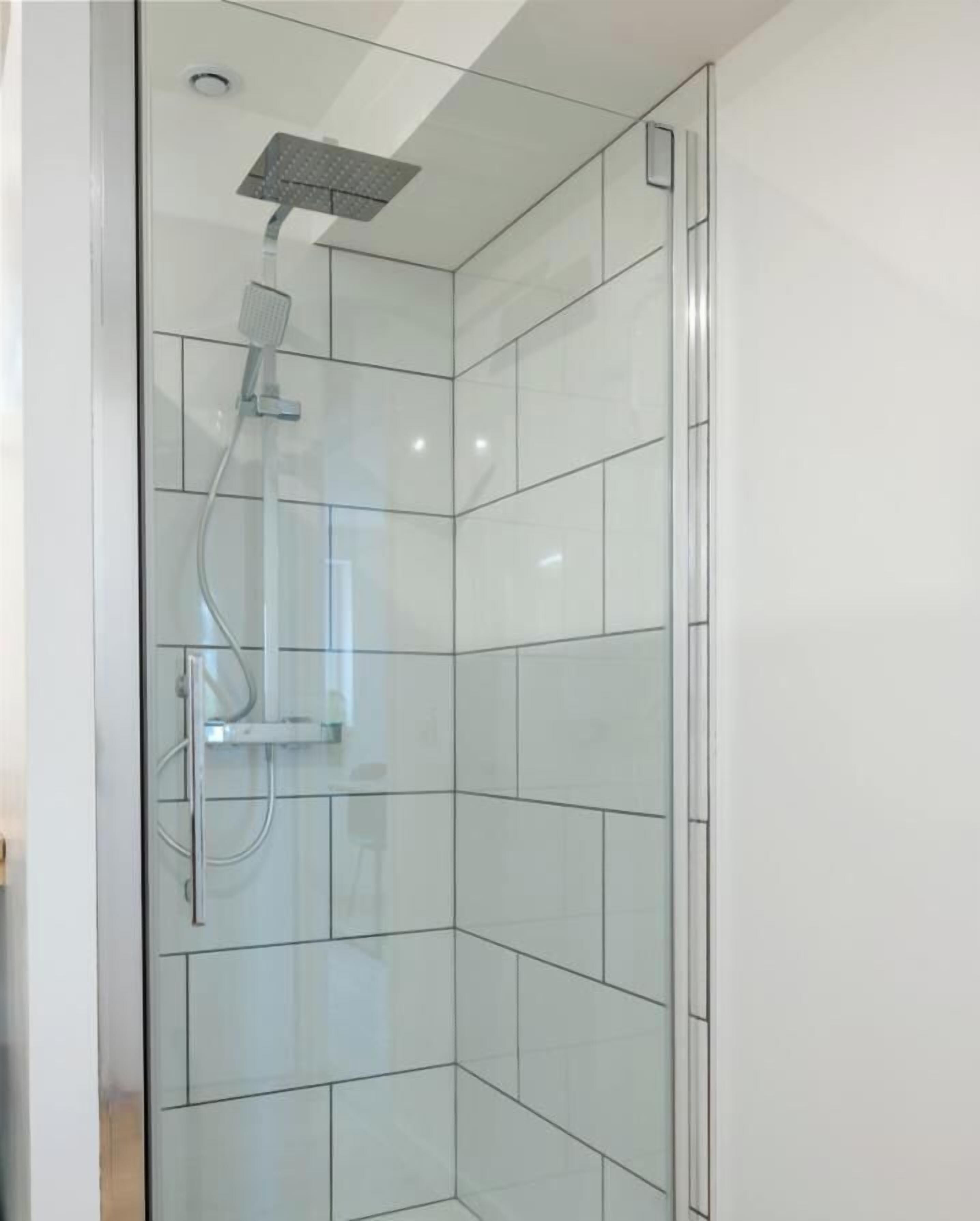 A glass-enclosed shower with a handheld showerhead and a wall-mounted control panel.