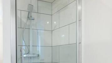 Een douchecabine met glazen wanden, een handdouche en een bedieningspaneel aan de muur.