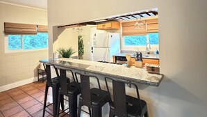 Una cocina con barra, taburetes negros, un refrigerador y una ventana con persianas.