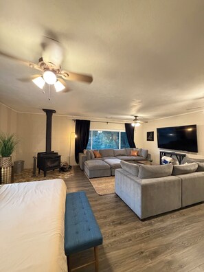 A modern living room with a large sectional sofa, a flat-screen TV, a ceiling fan, and a wood-burning stove. - Three Rivers Hideaway Near Sequoia National Park with Mountain View’s (Three Rivers)