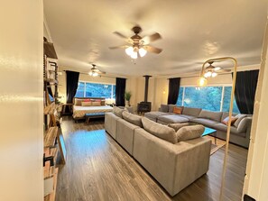 Ein modernes Wohnzimmer mit einer großen Eckcouch, einem Bett mit Kopfteil, einem Kamin und einem Deckenventilator.