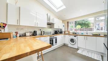 A modern kitchen with white cabinets, a wooden countertop, a skylight, a washing machine, and a window with a view of the outside.