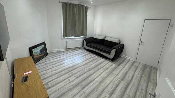 A room with a sofa, a TV, a wooden table, a radiator, and a door. - 4-Bed House - Ensuite Rooms - Sleeps 8 - Parking (Manchester)