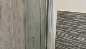 A bathroom with a glass shower door, a marble wall, and a tiled wall with a wood-like pattern. - 4-Bed House - Ensuite Rooms - Sleeps 8 - Parking (Manchester)