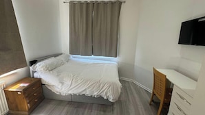 A bedroom with a bed, a wooden dresser, a desk, a television, and a window with curtains. - 4-Bed House - Ensuite Rooms - Sleeps 8 - Parking (Manchester)