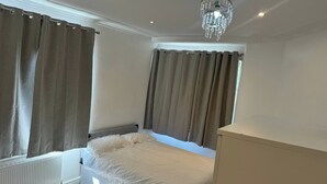 A bedroom with a bed, curtains, a radiator, and a chandelier. - 4-Bed House - Ensuite Rooms - Sleeps 8 - Parking (Manchester)