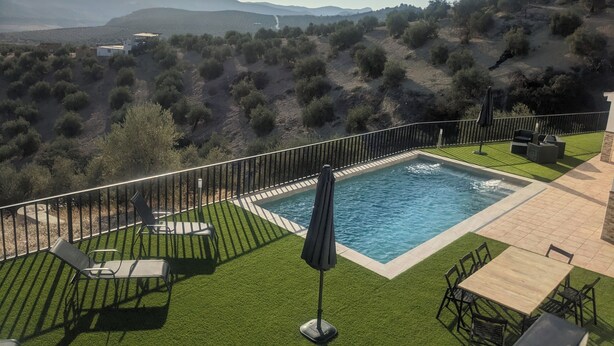 Ein Pool mit Blick auf Hügel und eine umzäunte Terrasse mit Stühlen und Tisch.