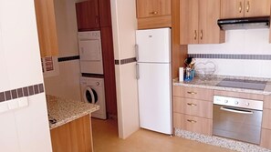 Eine kleine Küche mit Waschmaschine, Kühlschrank, Herd und Holzschränken.