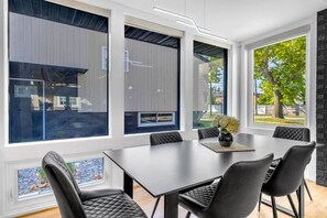 A modern dining area with a large table and chairs, large windows, and a view of the outdoors. - Elmhurst 4BR Home with Pool | Mid-Term Ready (Elmhurst)