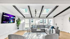 Una sala de estar moderna con un sofá modular, un televisor de pantalla plana montado en la pared, tragaluces y una planta en maceta.