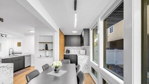 Una cocina moderna con encimeras de mármol, un comedor con mesa de madera oscura y un amplio ventanal con vistas al exterior.