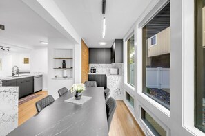 A modern kitchen with marble countertops, a dining area with a dark wooden table, and a large window with a view of the outdoors. - Elmhurst 4BR Home with Pool | Mid-Term Ready (Elmhurst)