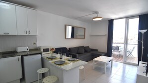A compact living space with a kitchenette, a dining area, a sofa, and a balcony with a view. - SYMAR BAJO - VISTAS AL CANAL (Roses)
