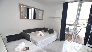 A hotel room with two beds, a desk, a chair, a window with curtains, and a balcony. - SYMAR BAJO - VISTAS AL CANAL (Roses)