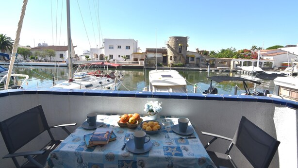A dining area with a table set for two, a view of the marina, and boats docked in the background. - SYMAR BAJO - VISTAS AL CANAL (Roses)