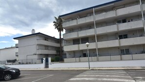 A multi-story building with balconies, a parking lot, and a palm tree. - SYMAR BAJO - VISTAS AL CANAL (Roses)