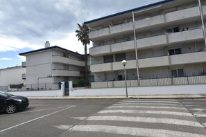 A multi-story building with balconies, a parking lot, and a palm tree. - SYMAR BAJO - VISTAS AL CANAL (Roses)