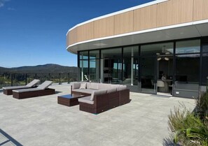 A modern building with a curved facade, outdoor seating area with lounge chairs and a sofa, and a glass entrance.