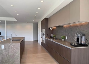 A modern kitchen with a marble island, wooden cabinets, and a built-in coffee machine.